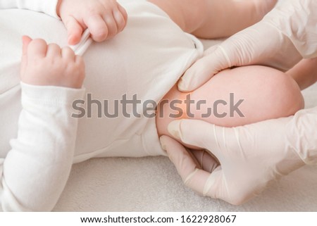 Doctor hands in white rubber protective gloves putting adhesive bandage on infant leg after injection of vaccine. Medical concept. Closeup.  Royalty-Free Stock Photo #1622928067