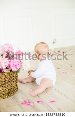 Cute little baby in a bright spring studio decorated with pink and white peonies