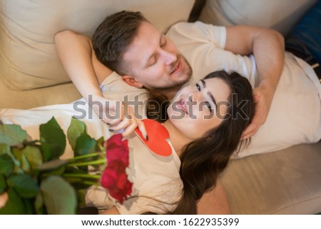 lovely couple hugging on the sofa, she holds roses, handsome husband tenderly strokes his beautiful wife's hair , happy romantic unniversary, saint valentine's day