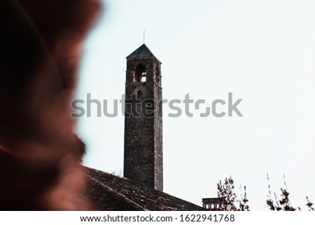 Stone bell tower of an old church in Pocitelj, Bosnia and Herzegovina. Palm tree blurred in foreground, intentionaly obscuring the frame, concept of religion. Muslim, christian and orthodox town.