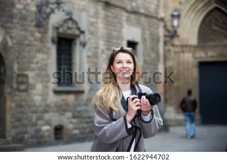 Happy  young girl holding camera in hands and photographing in the city