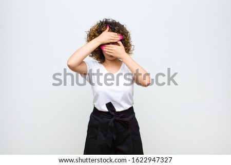young pretty woman covering face with both hands saying no to the camera! refusing pictures or forbidding photos against white wall