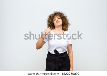 young pretty woman looking arrogant, successful, positive and proud, pointing to self against white wall
