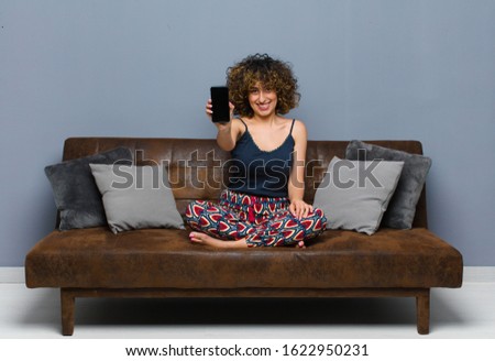young pretty woman at home, with a mobile phone, wearing pajamas on a sofa