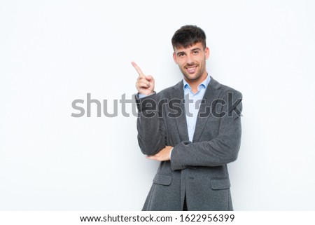 young handsome man smiling happily and looking sideways, wondering, thinking or having an idea against white wall