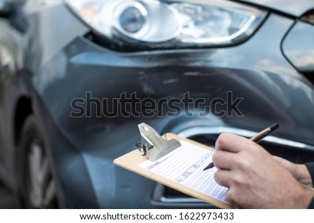 Close Up Of Auto Workshop Mechanic Inspecting Damage To Car And Filling In Repair Estimate Royalty-Free Stock Photo #1622973433