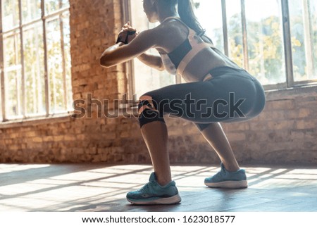 Young fit sporty active athlete woman wear sportswear crouching doing squats session fitness training legs buttocks muscles workout exercise in modern sunny gym space indoors, rear back close up view Royalty-Free Stock Photo #1623018577