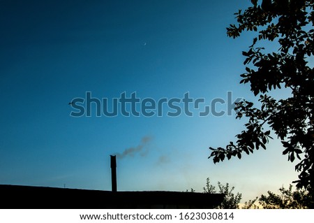 blue sky, a plane flying in the distance and a roof with a Smoking chimney in the foreground