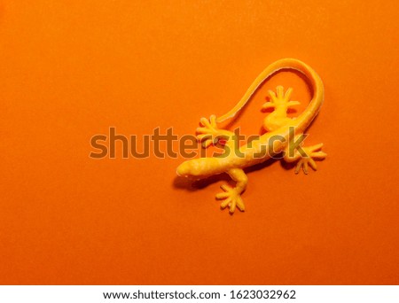 Rubber yellow lizard on a bright contrasting orange background with copy space, top view
