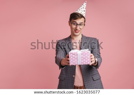Image of a young guy in glasses holding birthday present gift box isolated over pink wall background.