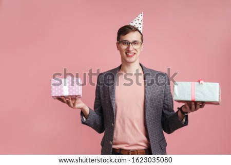 Image of a cheerful young boy in glasses holding birthday present gift boxes isolated over pink wall background.