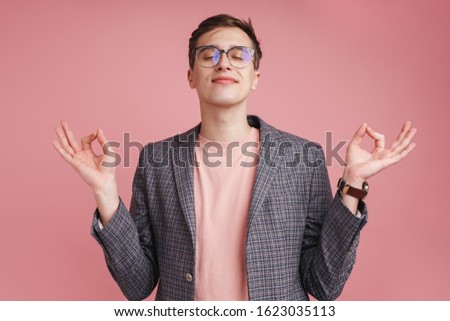 Photo of a young concentrated boy in glasses isolated over pink wall background make meditate calm gesture.