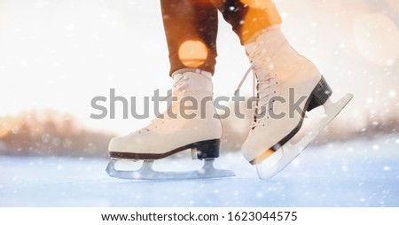 Girl is standing on ice in white figure skates, snow flakes, sunlight. Winter active vacation concept.