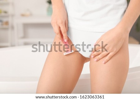 Beautiful young woman shaving bikini area in bathroom, closeup
