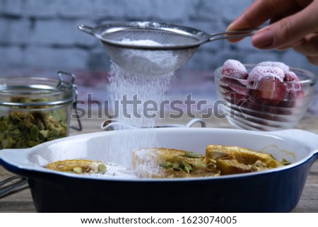 Caramelized apples with honey and cinnamon in a clay bowl hand sprinkles with powdered sugar on a light wooden background. Top views