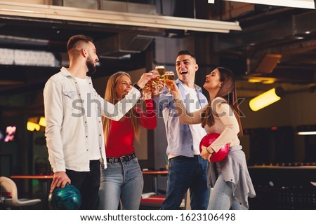Group of friends toast with a beer in a bowling alley