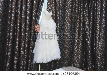 funny young man behind wedding dress and curtain
