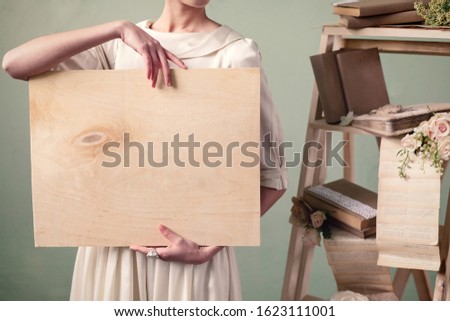 Woman holding a wood board. Frame for text. Vintage books and flowers on the shelf. Wedding mockup.