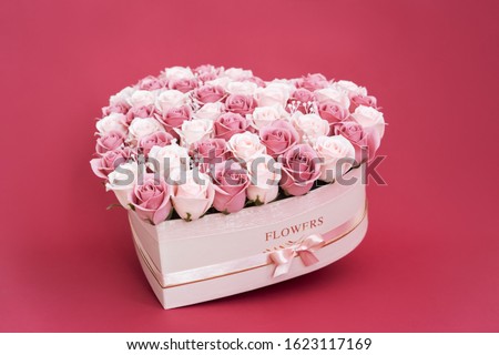 Flowers in bloom: A large bouquet of pink and white roses in a box in the shape of a heart on a pink background.