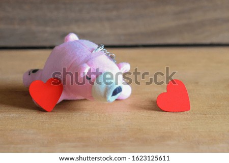 Red hearts with pink bear toy on wood table.