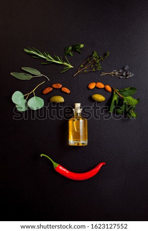 Picture smiling face making from herbs and bottle of essential oil on black background, top view, flat lay