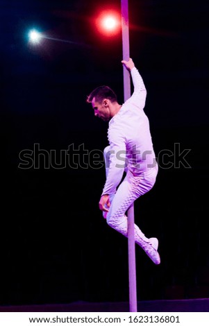 acrobat holding pole while performing near red and blue back light on black