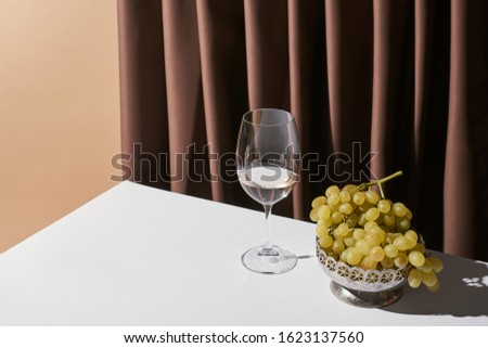 classic still life with grape and white wine on table near curtain isolated on beige