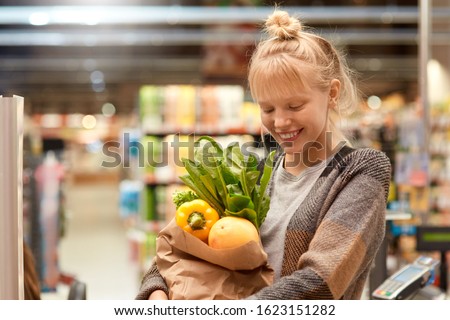 Young woman at the supermarket standing holding paper bag with shoppings fresh organic vegetables looking down laughing happy close-up just walk out shopping technology Royalty-Free Stock Photo #1623151282