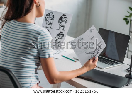 cropped view of illustrator holding papers with sketches