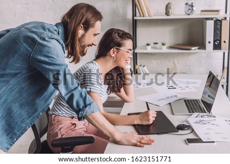 side view of animator looking at laptop near coworker and sketches