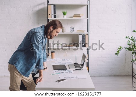 side view of illustrator looking at sketches in studio
