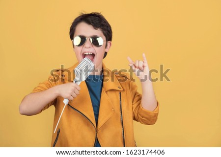 child with sunglasses holding a microphone doing rock symbol with hands up 