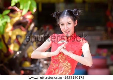 A beautiful Asian woman takes a picture in a Chinese costume, showing a traditional salute for the Chinese New Year