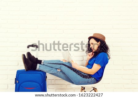 Cute girl holding map and choose a route of travel. Woman with suitcase ready to travel. Young woman chooses a place to travel using map sitting in office travel agency. Vacation and holidays