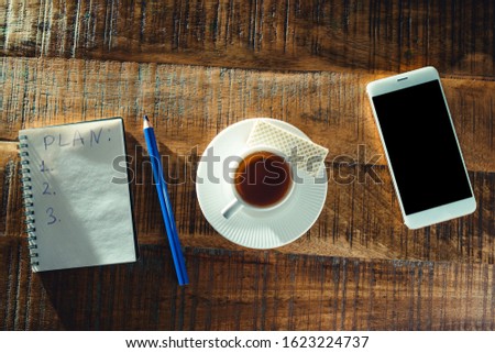 Morning coffee with notebook and action plan on wooden desk, top view. Cup of coffee or tea for mood. Morning coffee mug, empty notebook, pencil and smartphone, flat lay