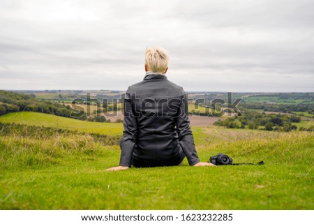 Blond woman with camera aside contemplating hilly green landscape