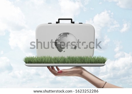 Side view of woman's hand holding ipad with green grass growing on screen, and white case with image of Earth's continents on, standing on grass. Global health. Sustainable development. Explore Earth.