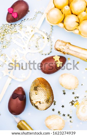Easter party theme image, conceptual image, golden egg. champagne, golden items with party  glasses,chocolate funny eggs on a blue background, top view,