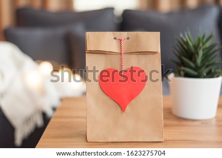 Heart Tag Paper Bag On The Coffee Table. Sofa In The Background. Valentine Day Favor Bag. Red Heart Mock Up. Valentines Day Concept. Valentine Identity Branding Mockup