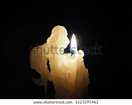 Isolated white candle with flame in the shape of an angel made of natural wax on a black background. Romantic picture of a burning candle for wallpaper, decoration and design closeup.