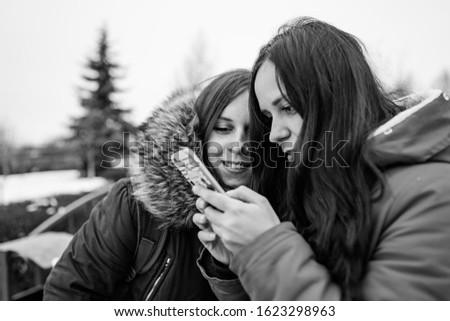 The meeting of girlfriends on street. Two women look in mobile phone, considering their photos on walk. Black and white photo.