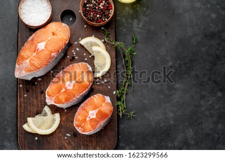 
fresh raw salmon steaks on a stone background with salt, pepper, lemon with copy space for your text