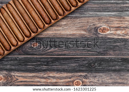 Cigars in wooden box on old table. Cigar manufacturing in vintage traditional scale tools, top view. Old box with handmade cigars in wooden humidor. Collection hand rolled cigar pre labelling Royalty-Free Stock Photo #1623301225
