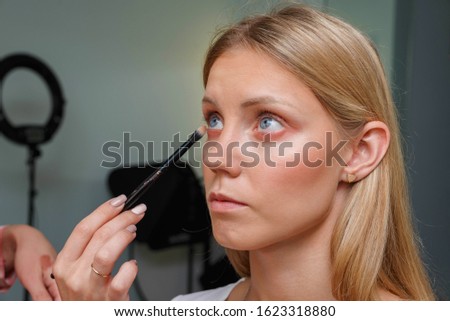 The process of creating makeup. Makeup artist working with a brush on the face of the model. Portrait of a young woman in the interior of a beauty salon. Applying tone to the skin.