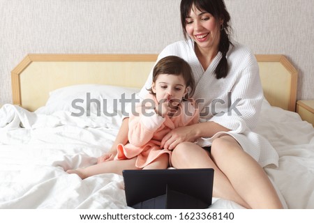 Mother and daughter using tablet and watching movie. Girl pick her nose and take a snivel, motehr is laughing. 
