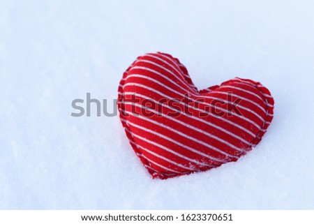 Homemade textile soft heart of red color with white stripes on the cold snow in winter.  Selective focus. A gift for Valentine's day. Lonely heart
