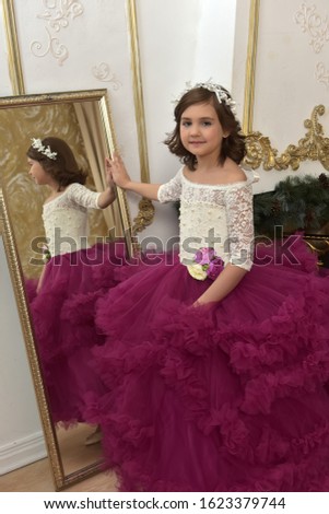 a girl in a chic white dress with a burgundy dress stands by the mirror and looks at her reflection