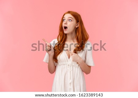 Wow look at that. Speechless and intrigued, curious excited redhead girl seeing something awesome, drop jaw, gasping and observe interesting performance, standing pink background