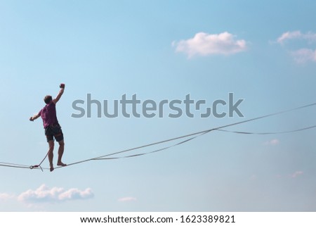 Highliner on the background of blue sky makes a move. A man is walking along a stretched sling. Performance tightrope walker. Man balances over the abyss. A decisive step forward.