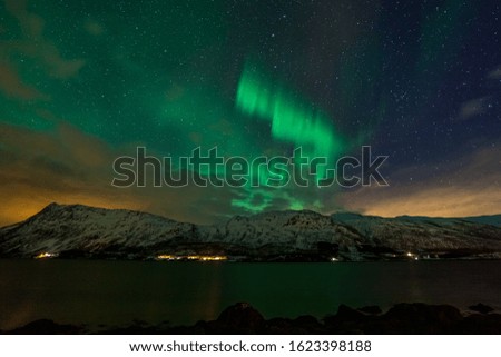beautiful aurora borealis, northern lights over fjord mountains with many clouds in the sky in the North of Europe , Lofoten islands, Norway, long shutter speed.